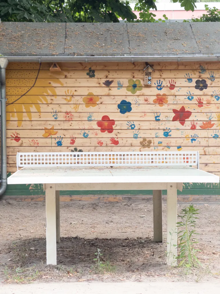 Tischtennisplatte vor einer von Kindern bemalten Wand mit Blumen und Handabdrücken