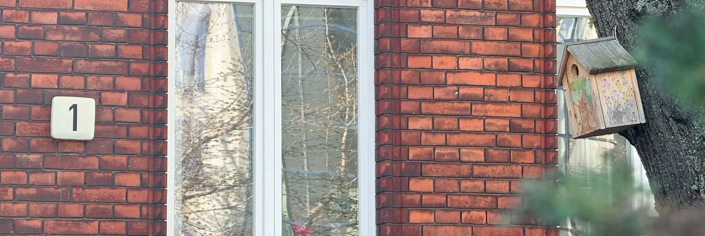 Hausnummer 1 an der Backsteinfassade des Pfarrhauses, daneben ein von Kindern bemalter Nistkasten